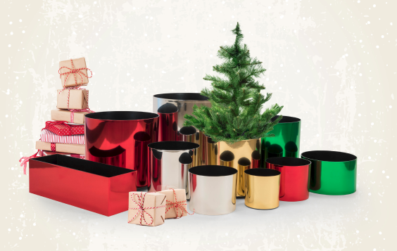 a holiday planter arrangement of red, green, silver and gold round planters with an evergreen tree and stack of presents in a corner
