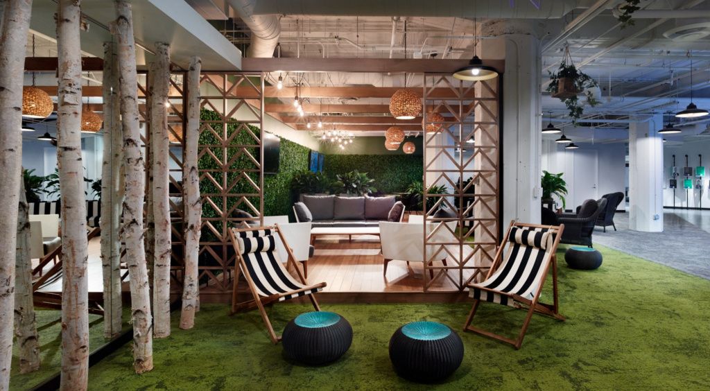 interior office with tree trunk columns, plant wall, grassy green carpet and striped folding chairs as an example of biophilic design in the workplace